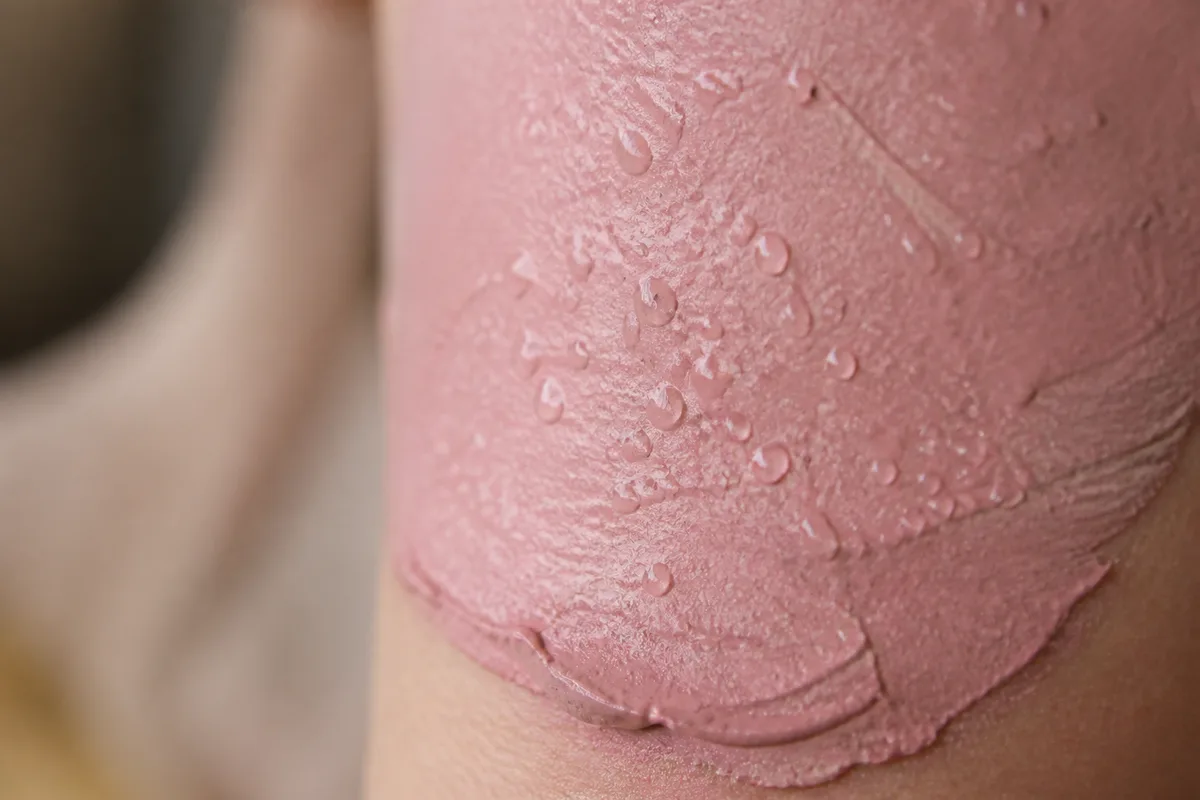 Masque d&rsquo;argile rose appliqué en couche épaisse sur une joue, gouttelettes d&rsquo;eau vaporisées en surface