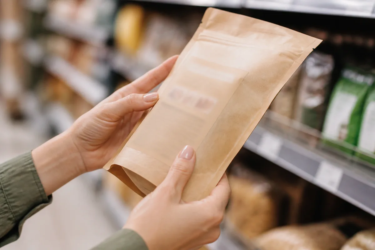 Mains tenant un sachet de preparation patissiere devant un rayon de magasin, etiquette illisible