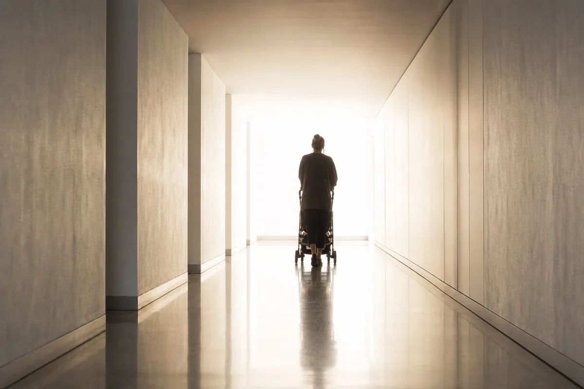 Silhouette d’un parent de dos poussant une poussette dans un long couloir baigné de lumière