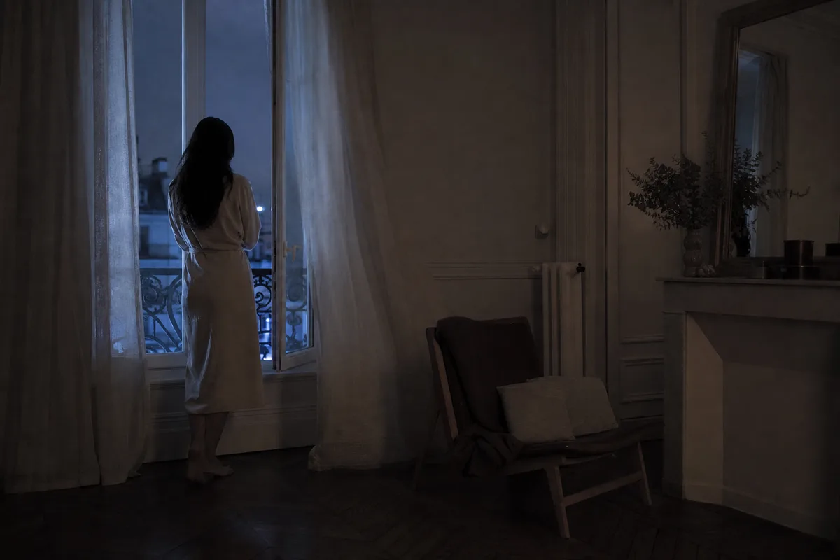 Silhouette de dos près d&rsquo;une fenêtre entrouverte au milieu de la nuit